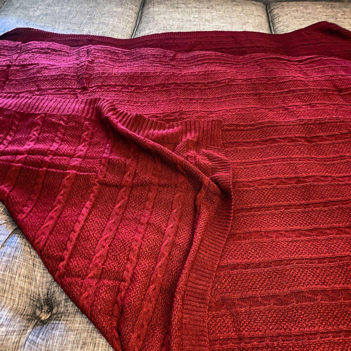 Claret Cotton-Blend Cable-Knit Throw: Red cable-knit throw with ribbed borders spread on a sofa.