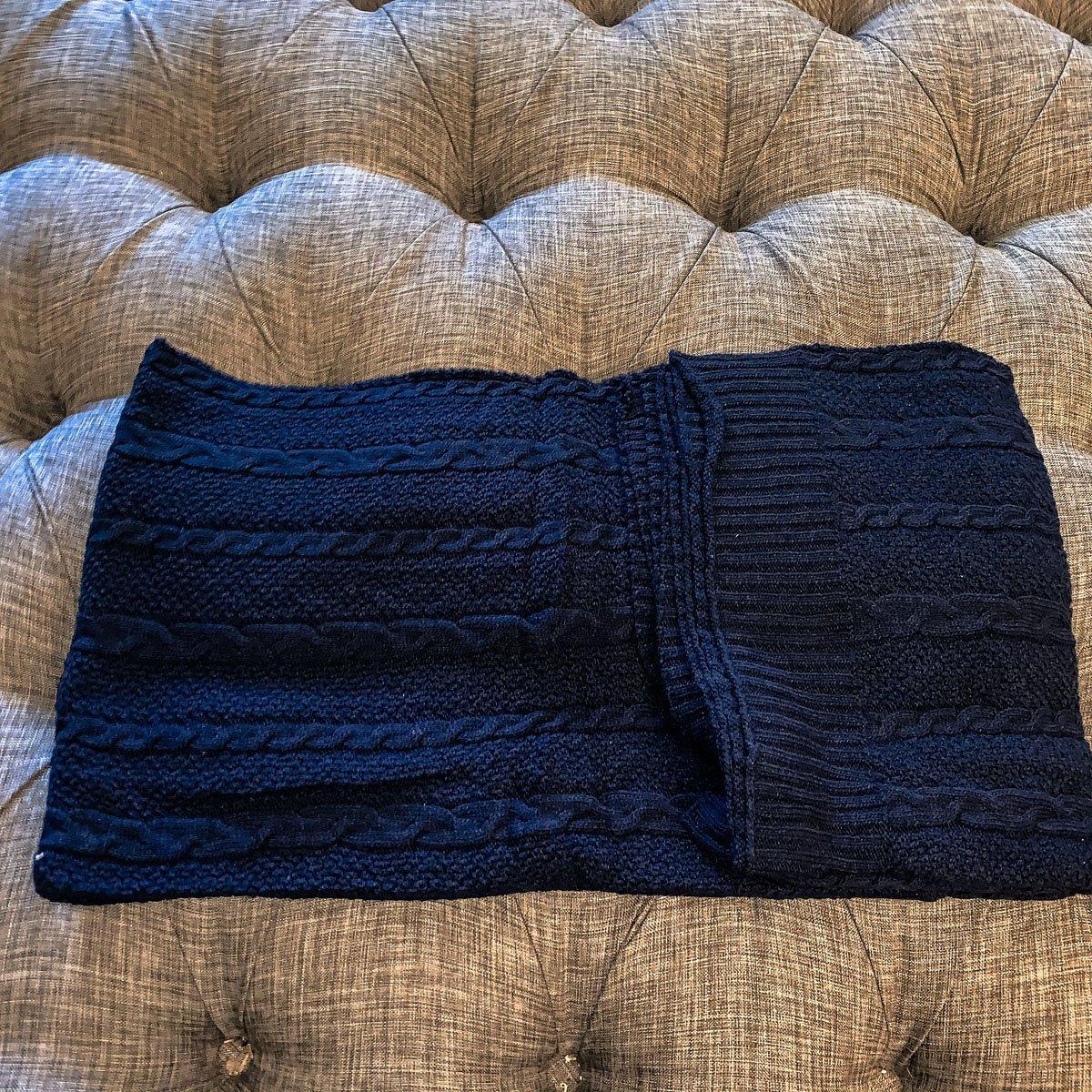 Claret Cotton-Blend Cable-Knit Throw: Blue cable-knit throw folded across a tufted sofa.