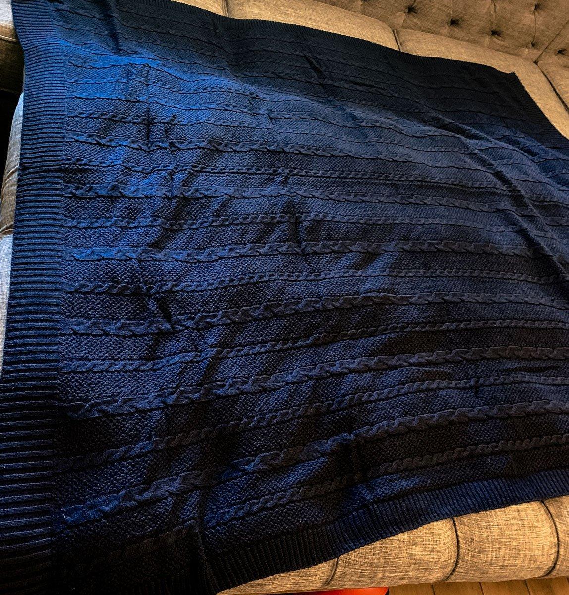 Claret Cotton-Blend Cable-Knit Throw: Blue cable-knit throw spread on a wooden bench.