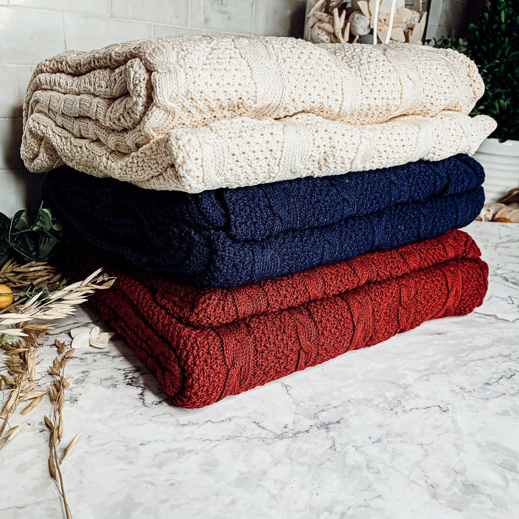 Claret Cotton-Blend Cable-Knit Throw: Stacked cable-knit throws in cream, blue and red.