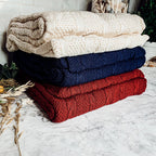 Claret Cotton-Blend Cable-Knit Throw: Stacked cable-knit throws in cream, blue and red.