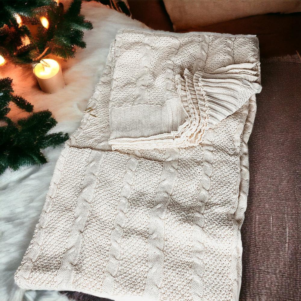 Claret Cotton-Blend Cable-Knit Throw: Cream cable-knit throw spread beside seasonal greenery.