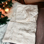 Claret Cotton-Blend Cable-Knit Throw: Cream cable-knit throw spread beside seasonal greenery.