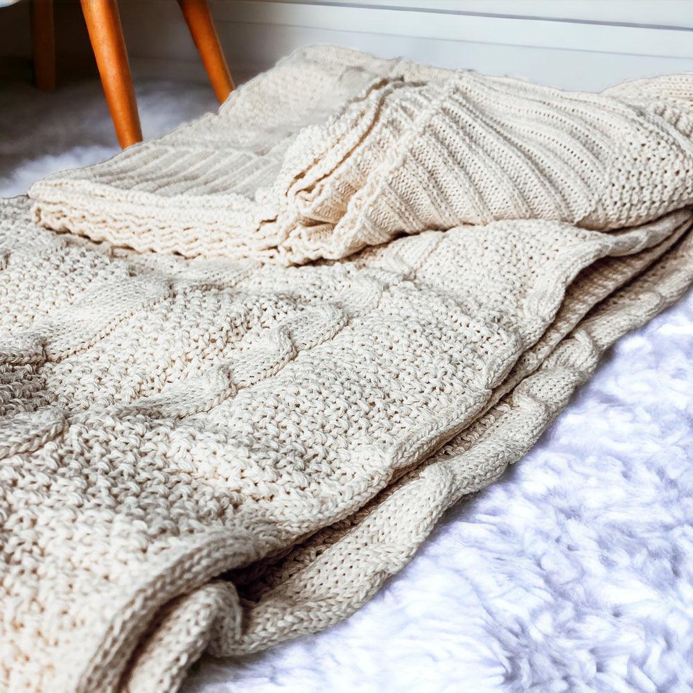 Claret Cotton-Blend Cable-Knit Throw: Cream cable-knit throw folded on an upholstered chair.