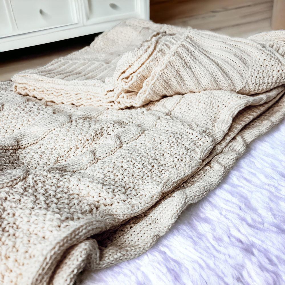 Claret Cotton-Blend Cable-Knit Throw: Cream cable-knit throw folded across an upholstered chair.