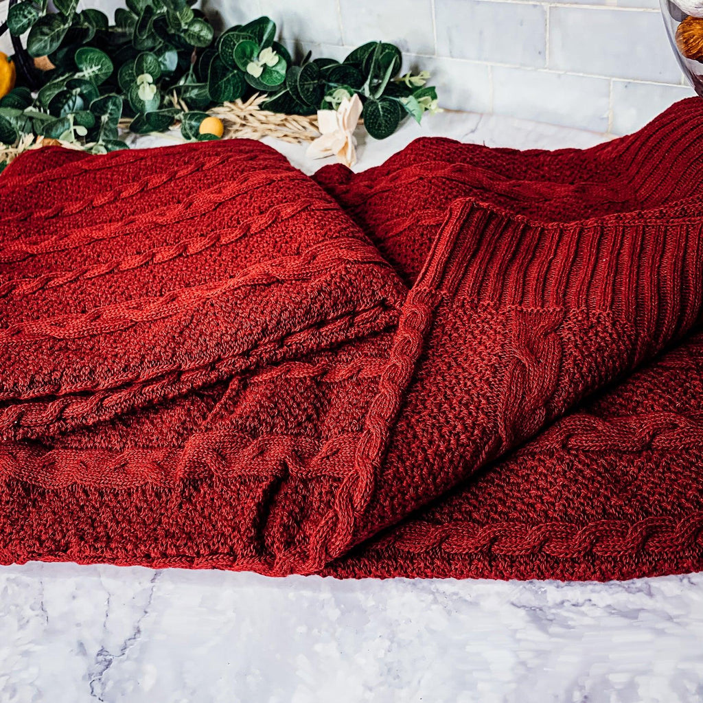 Claret Cotton-Blend Cable-Knit Throw: Close-up of red cable knitting and folded edge.