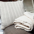 Claret Cotton-Blend Cable-Knit Throw: Cream cable-knit throw and matching textured cushion on a chair.