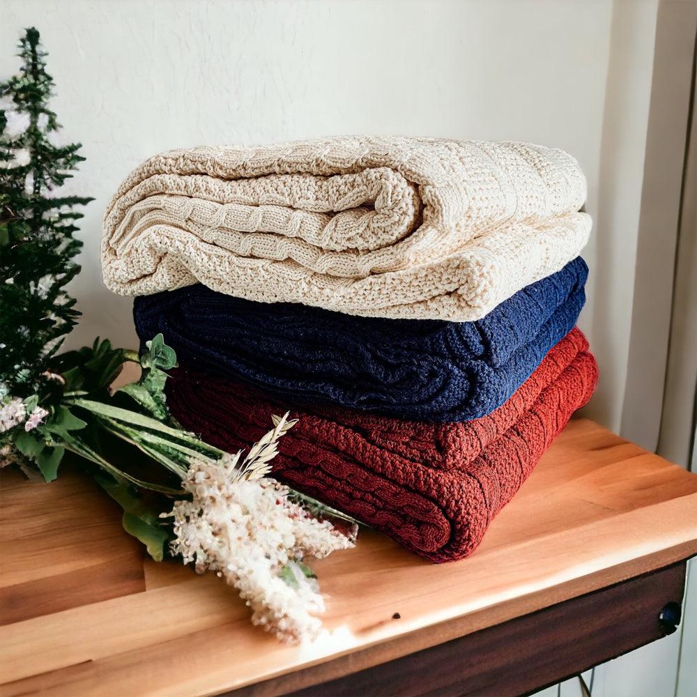Claret Cotton-Blend Cable-Knit Throw: Stack of folded cable-knit throws on a wooden chair.