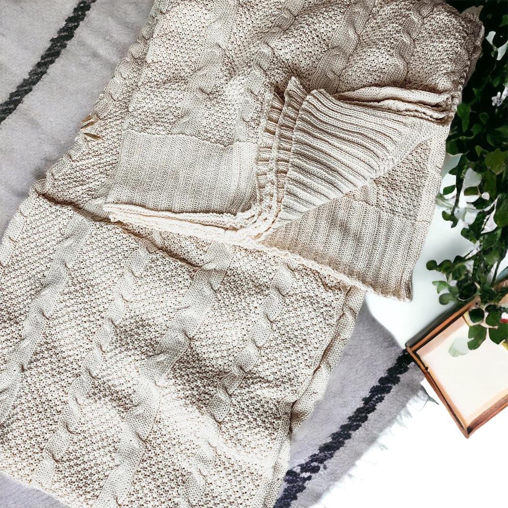 Claret Cotton-Blend Cable-Knit Throw: Cream cable-knit throw beside patterned fabric on a sofa.