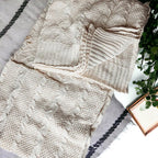Claret Cotton-Blend Cable-Knit Throw: Cream cable-knit throw beside patterned fabric on a sofa.