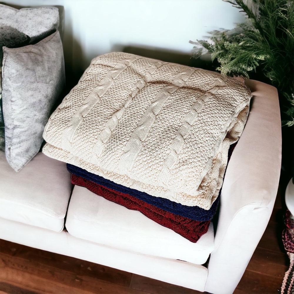 Claret Cotton-Blend Cable-Knit Throw: Cream throw folded over blue and red throws on a chair.