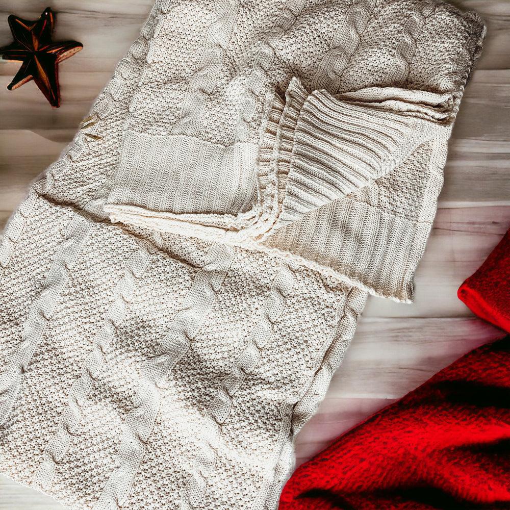 Claret Cotton-Blend Cable-Knit Throw: Cream cable-knit throw beside patterned fabric and autumn decorations.