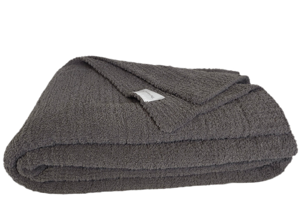 The Nest Microfiber Throw — 75 × 52 in: Folded dark throw with a visible fabric label.