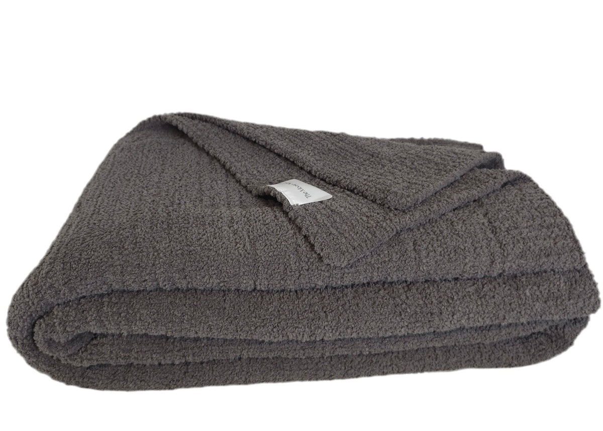 The Nest Microfiber Throw — 75 × 52 in: Folded dark throw with a visible fabric label.
