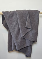 The Nest Microfiber Throw — 75 × 52 in: Gray throw folded over an upholstered backrest.