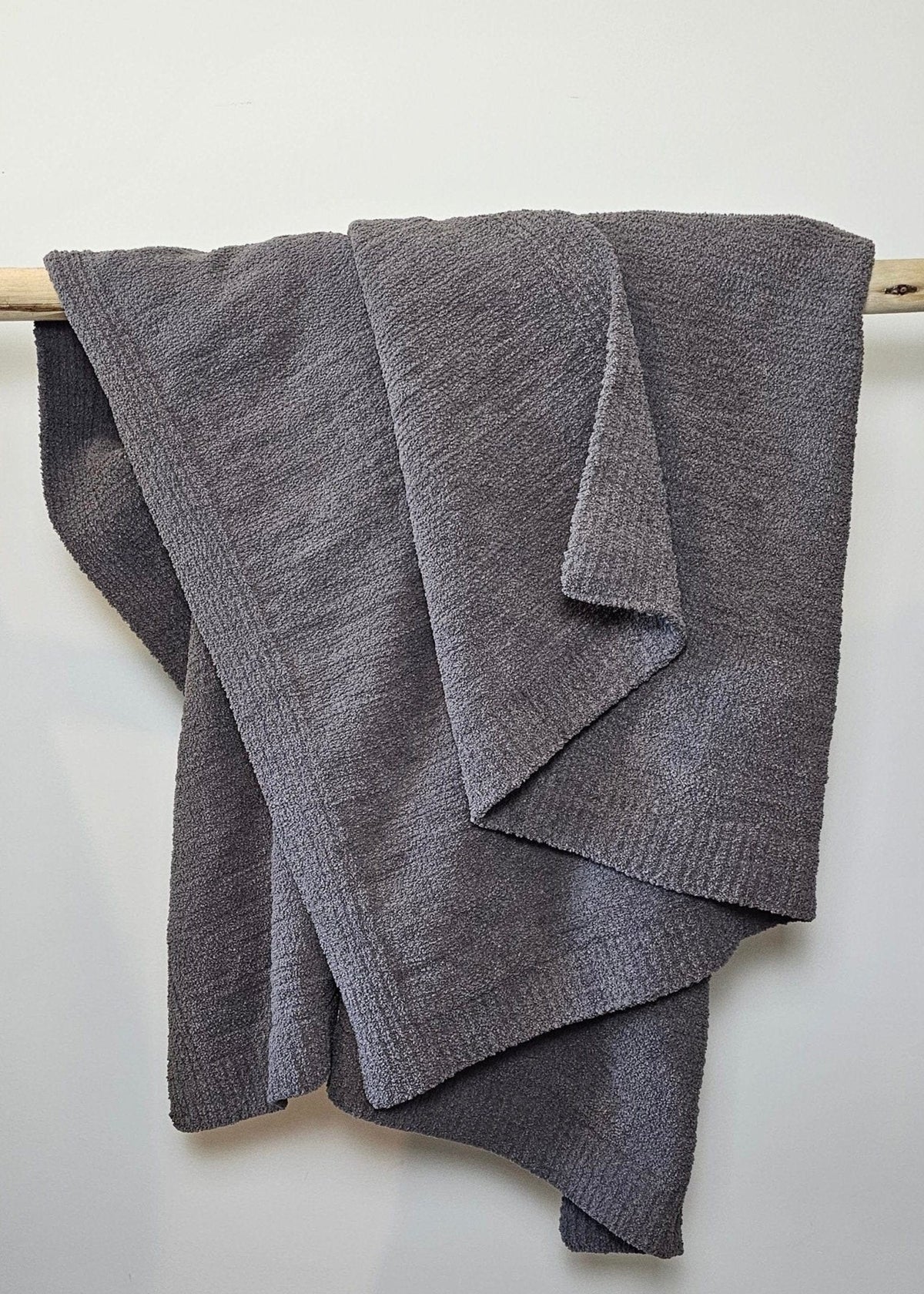The Nest Microfiber Throw — 75 × 52 in: Gray throw folded over an upholstered backrest.