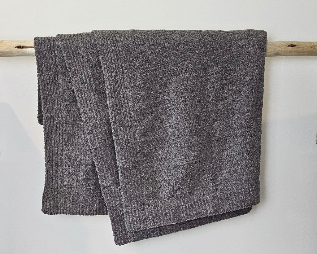 The Nest Microfiber Throw — 75 × 52 in: Gray throw draped over a light upholstered surface.