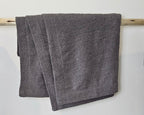 The Nest Microfiber Throw — 75 × 52 in: Gray throw draped over a light upholstered surface.
