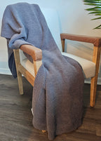 The Nest Microfiber Throw — 75 × 52 in: Gray throw draped over a wooden armchair.
