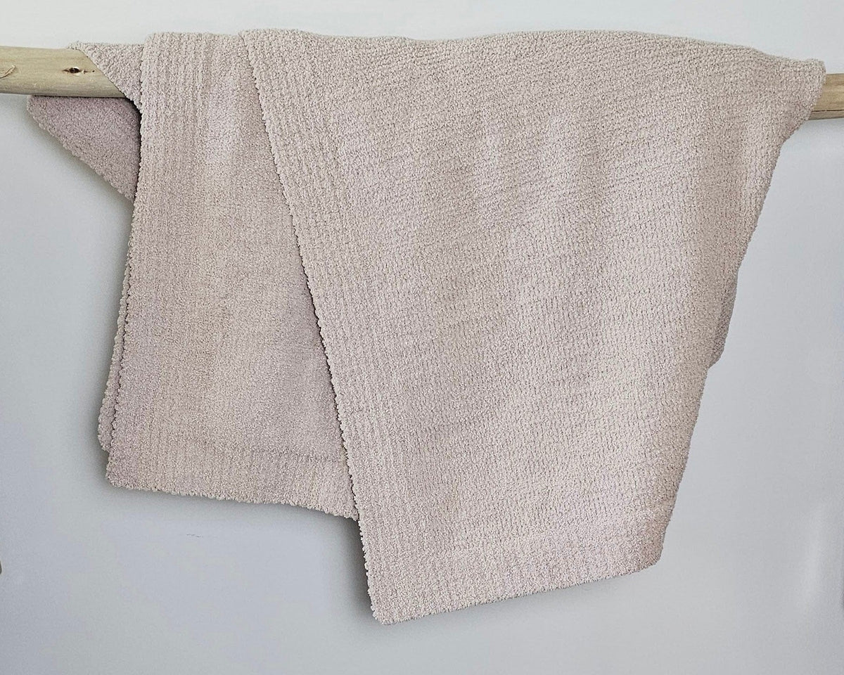 The Nest Microfiber Throw — 75 × 52 in: Beige throw folded over an upholstered backrest.