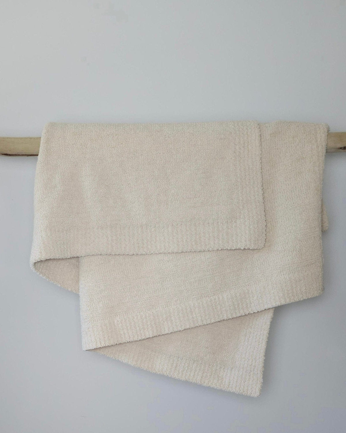 The Nest Microfiber Throw — 75 × 52 in: Cream throw folded over an upholstered backrest.